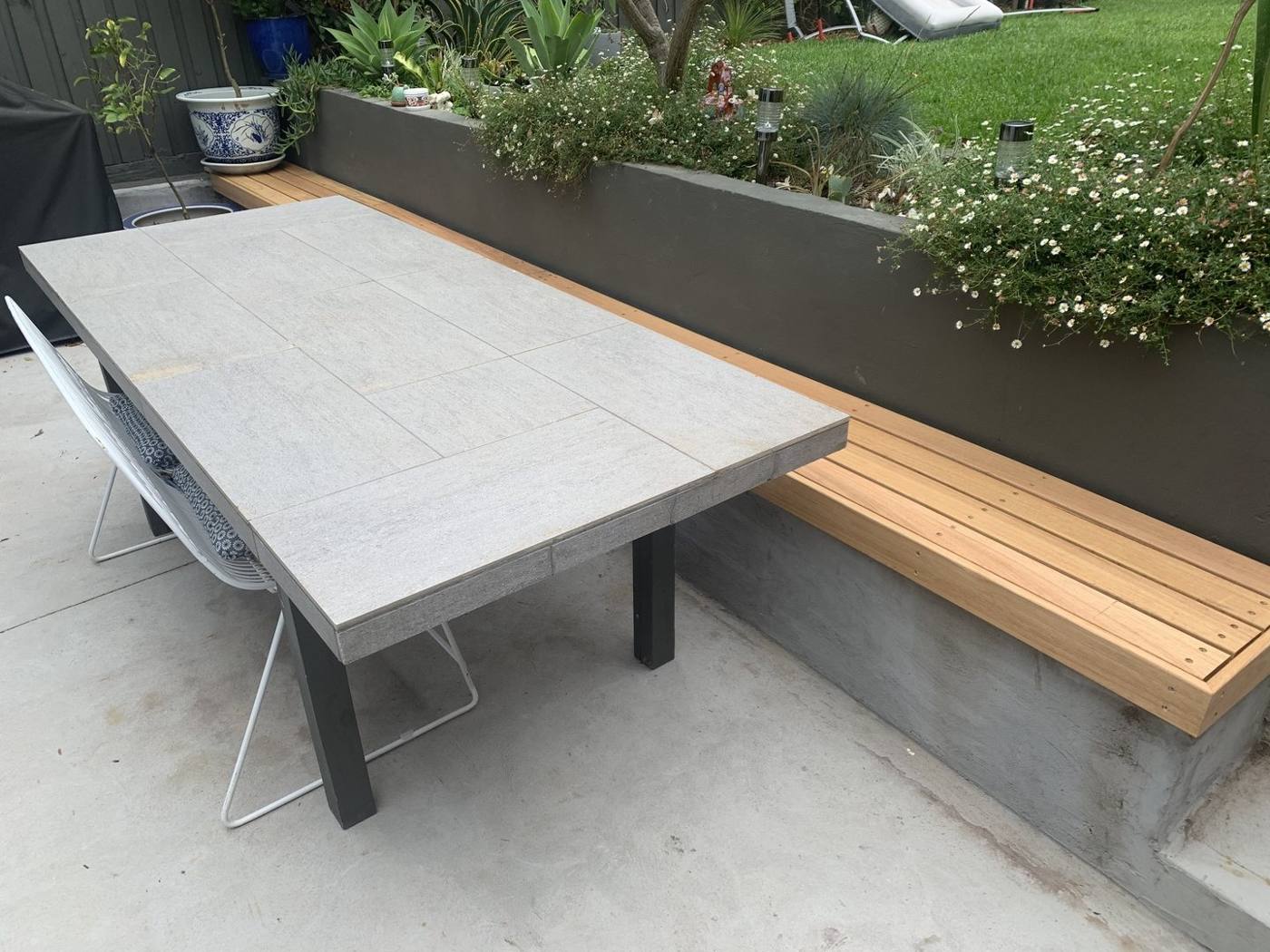 Courtyard dining setting with a tiled-top table beside the built-in timber bench and planter by Loel Homes