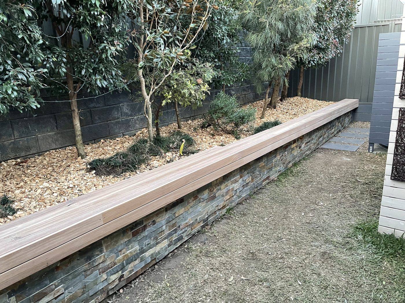 Finished timber bench running the full length of the stone planter wall with garden bed behind, courtyard by Loel Homes