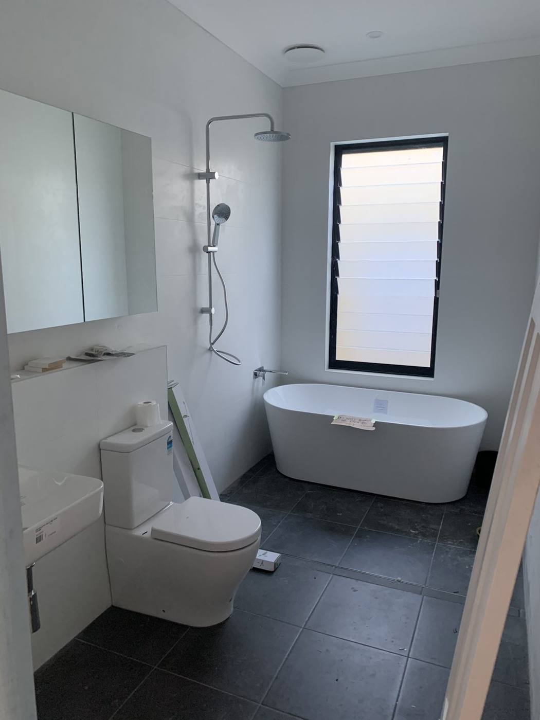 Finished bathroom with freestanding oval bath, rain shower, wall-hung vanity and black-framed louvre window, Dulwich Hill by Loel Homes