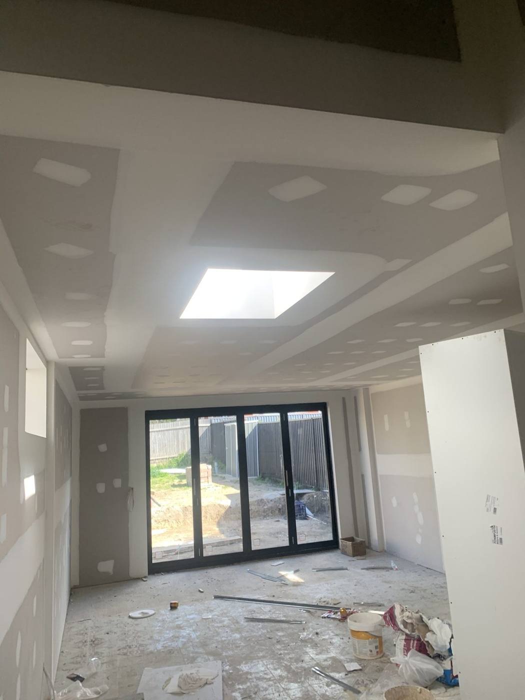 Open-plan living lined in plasterboard with skylight and bi-fold doors, Dulwich Hill by Loel Homes