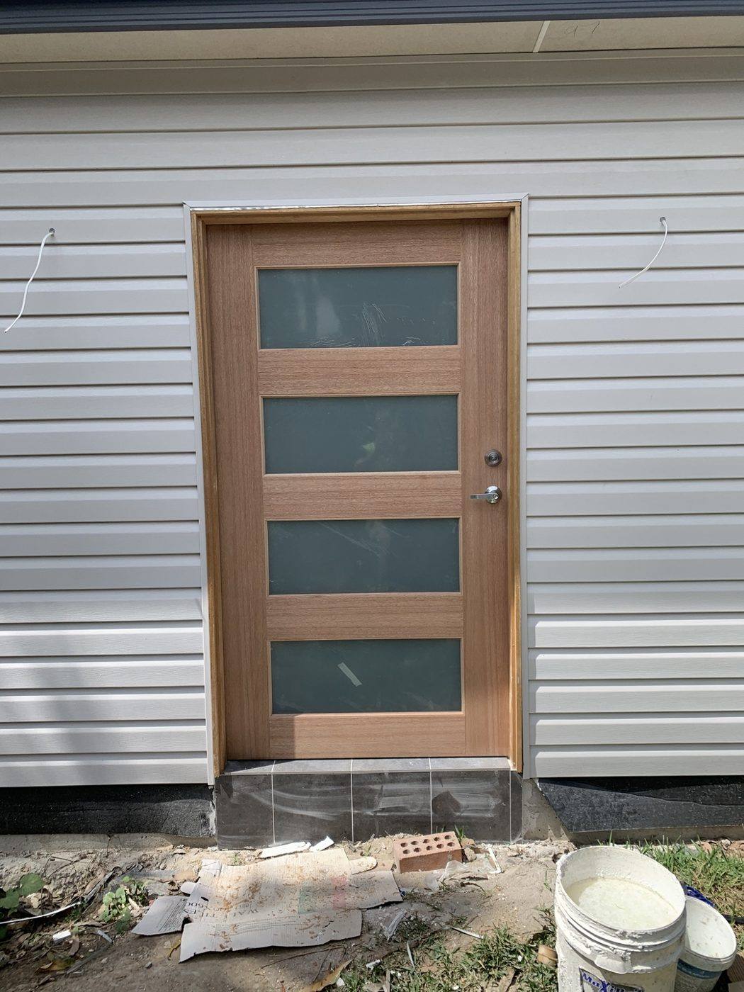 Natural timber four-slot frosted-glass front entry door on a weatherboard home, front view by Loel Homes