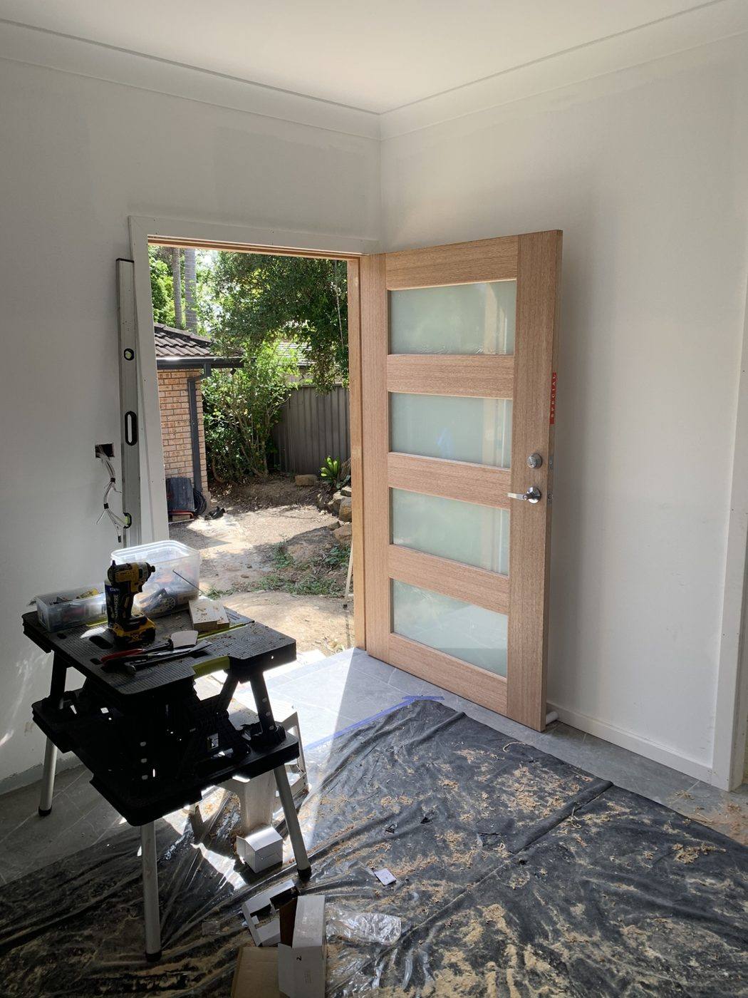 Natural timber four-slot front entry door swung open showing the hinges and the garden beyond by Loel Homes