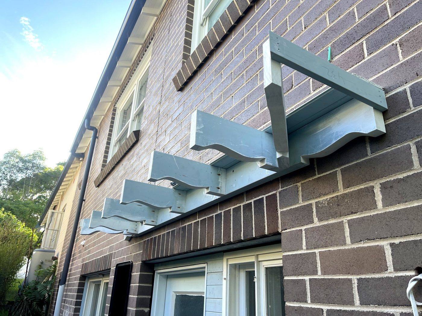 Shaped timber corbels and window awning frame fixed to a brick wall and primed grey on an Eastwood home by Loel Homes