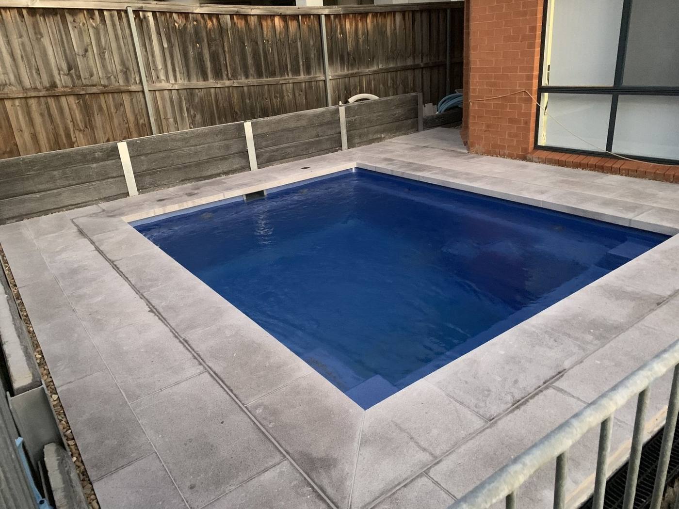 Completed backyard pool with paved surround and timber boundary fence by Loel Homes