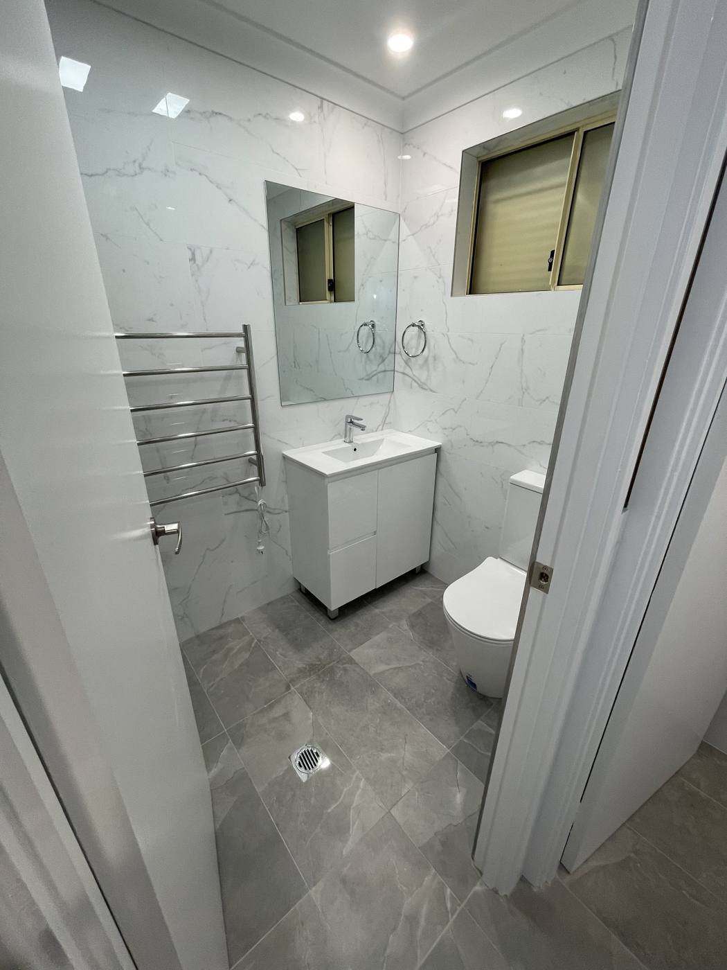 Finished modern bathroom after renovation with white vanity, heated towel rail, new toilet, mirror and marble-look walls, Quakers Hill by Loel Homes