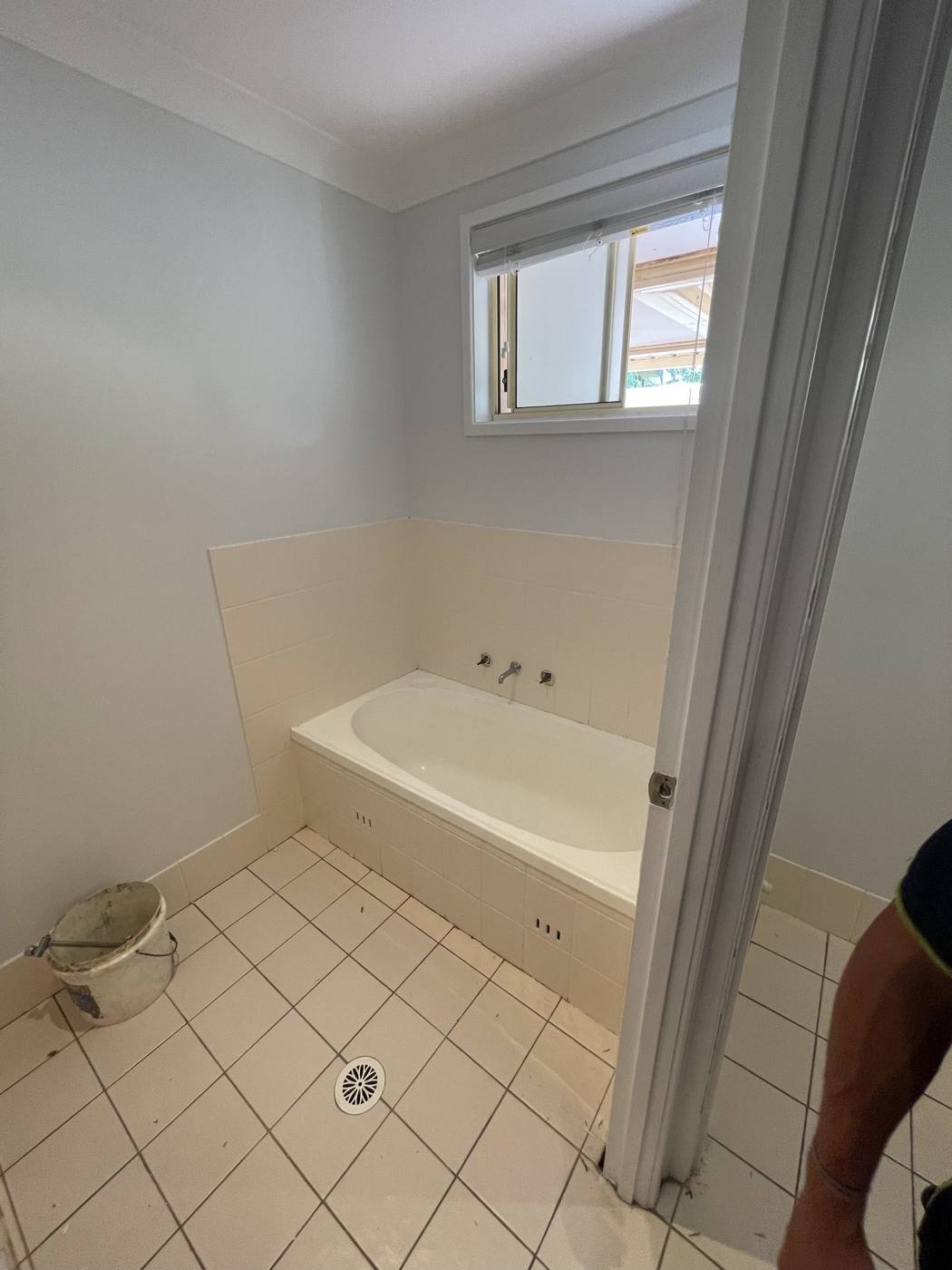 Bathroom mid strip-out during renovation with old bath and wall tiles being removed and a bucket on the floor, Quakers Hill by Loel Homes