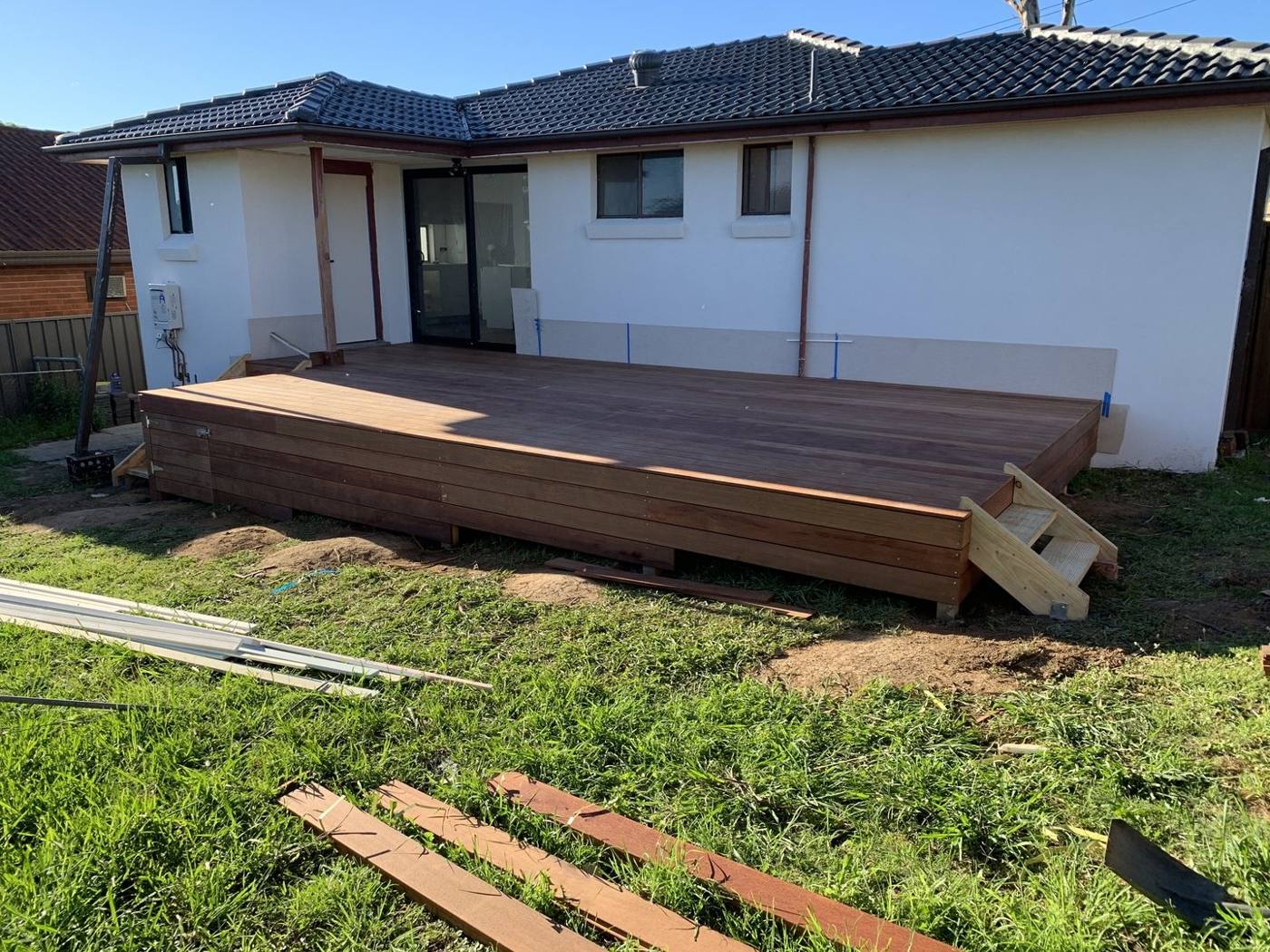 Finished low-line hardwood deck wrapping the rear of a rendered home with tiled roof by Loel Homes