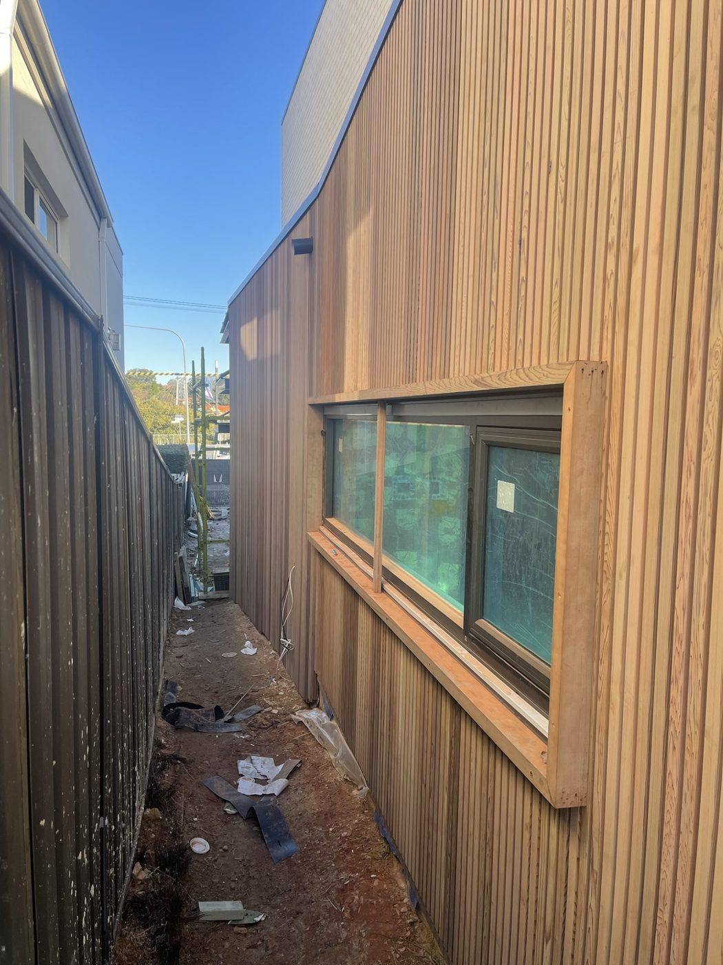 Timber-framed window set into pale battened cladding along a side passage, duplex by Loel Homes